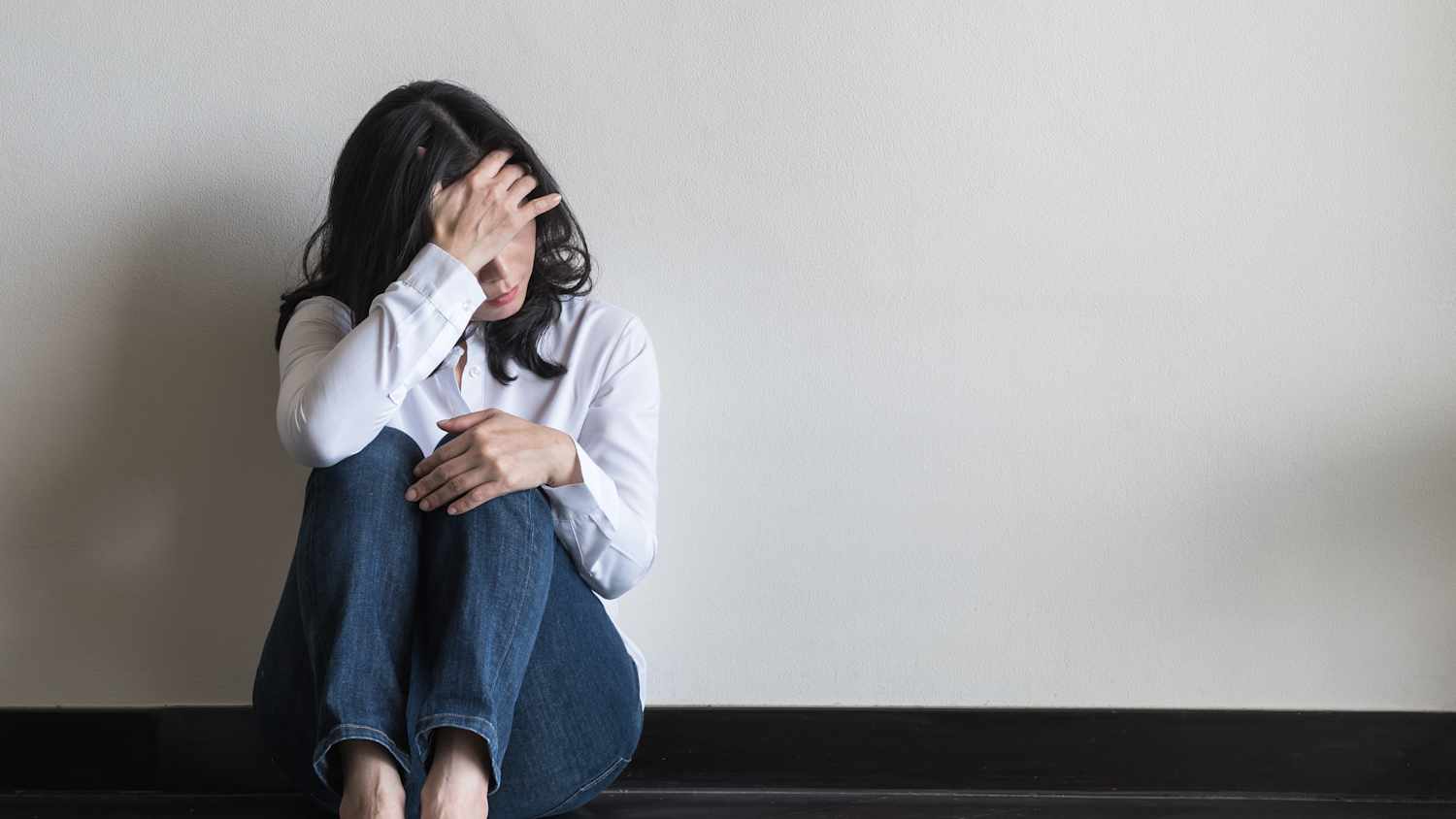 Eine Frau sitzt zu Hause auf dem Boden und stützt ihren Kopf auf ihre Hand