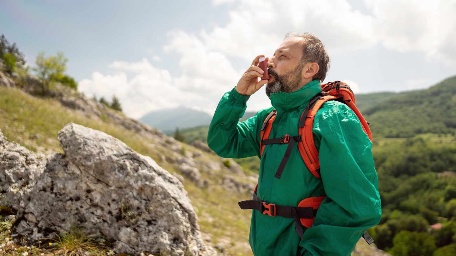 Ein Mann welcher in den Bergen unterwegs ist und an einem Asthmaspray zieht