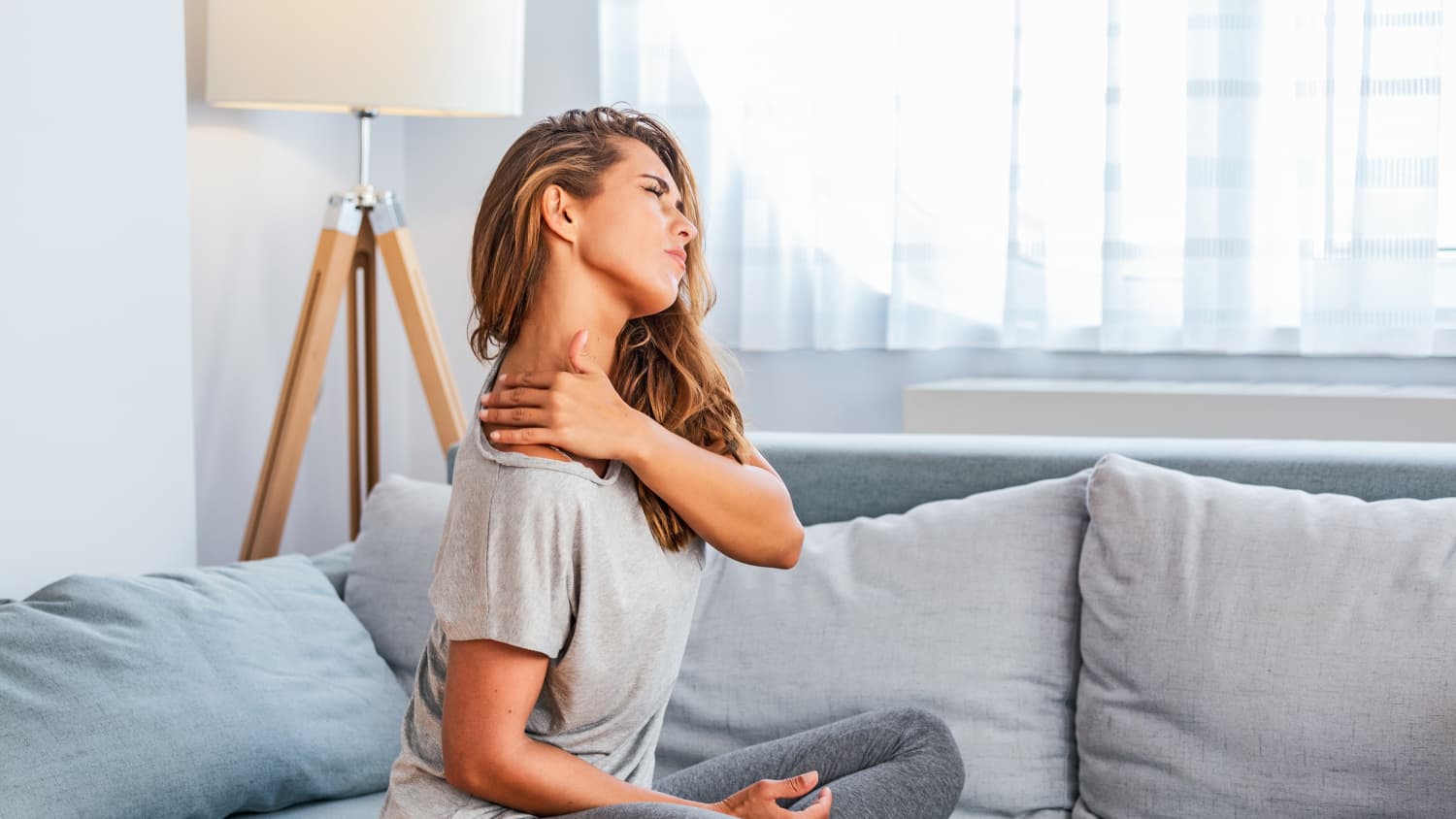 Eine Frau sitzt mit verspannten Rücken auf dem Sofa
