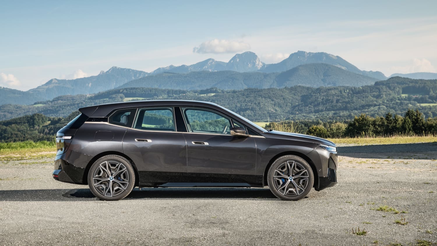 Der erste BMW iX in schwarz parkend, von der Seite vor einer Berglandschaft