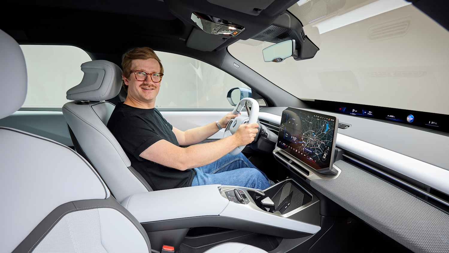 ADAC Redakteur Andreas Huber sitzt im Cockpit des BMW iX3 und hält das Lenkrad.