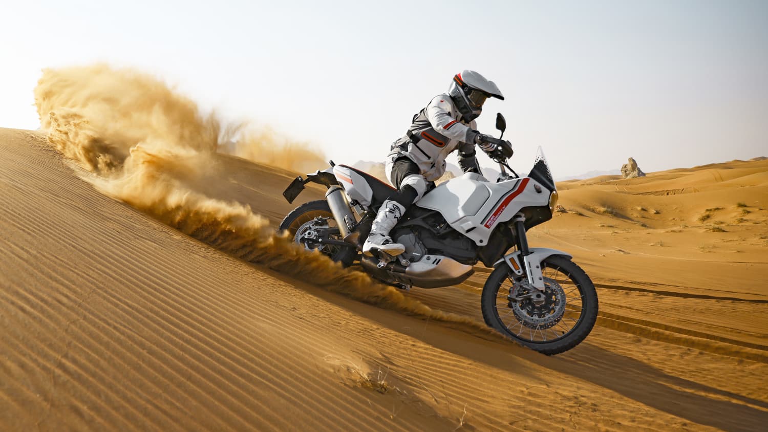 Seitenansicht einer durch die Wüste fahrenden Ducati Desert X