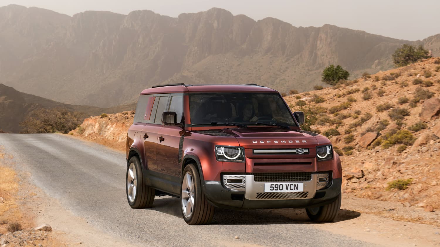 Ein weinroter Range Rover Defender in karger Wüstenlandschaft