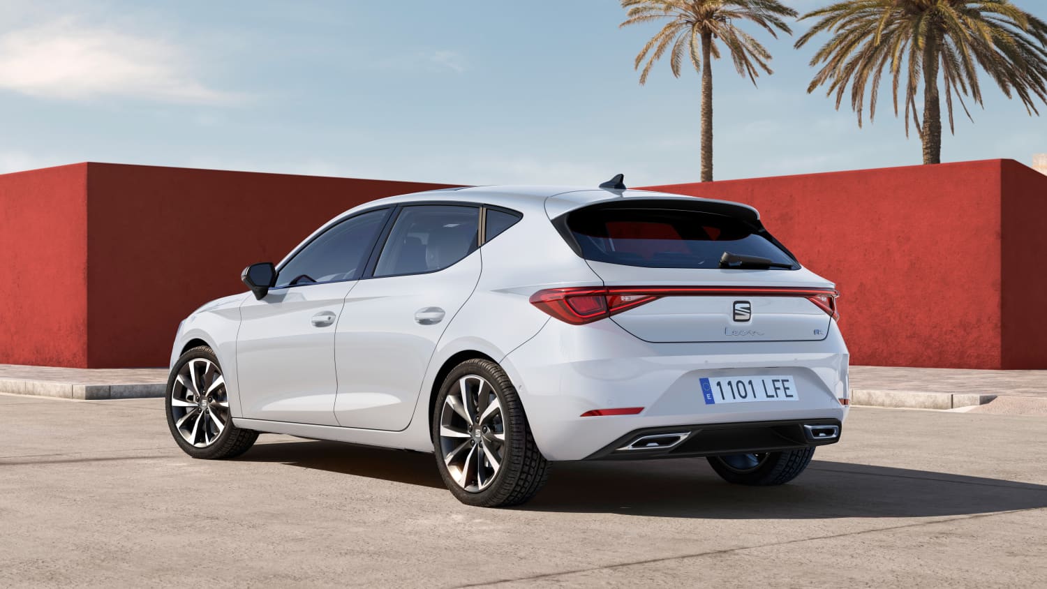 Die Rückansicht eines weißen Seat Leon vor einem roten Gebäude mit Palmen