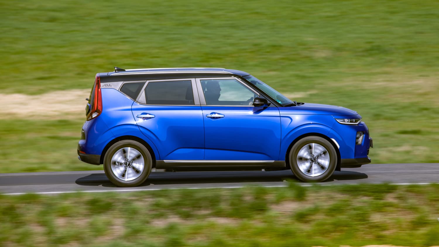 Blauer Kia E-Soul faehrt auf Strasse durch Landschaft