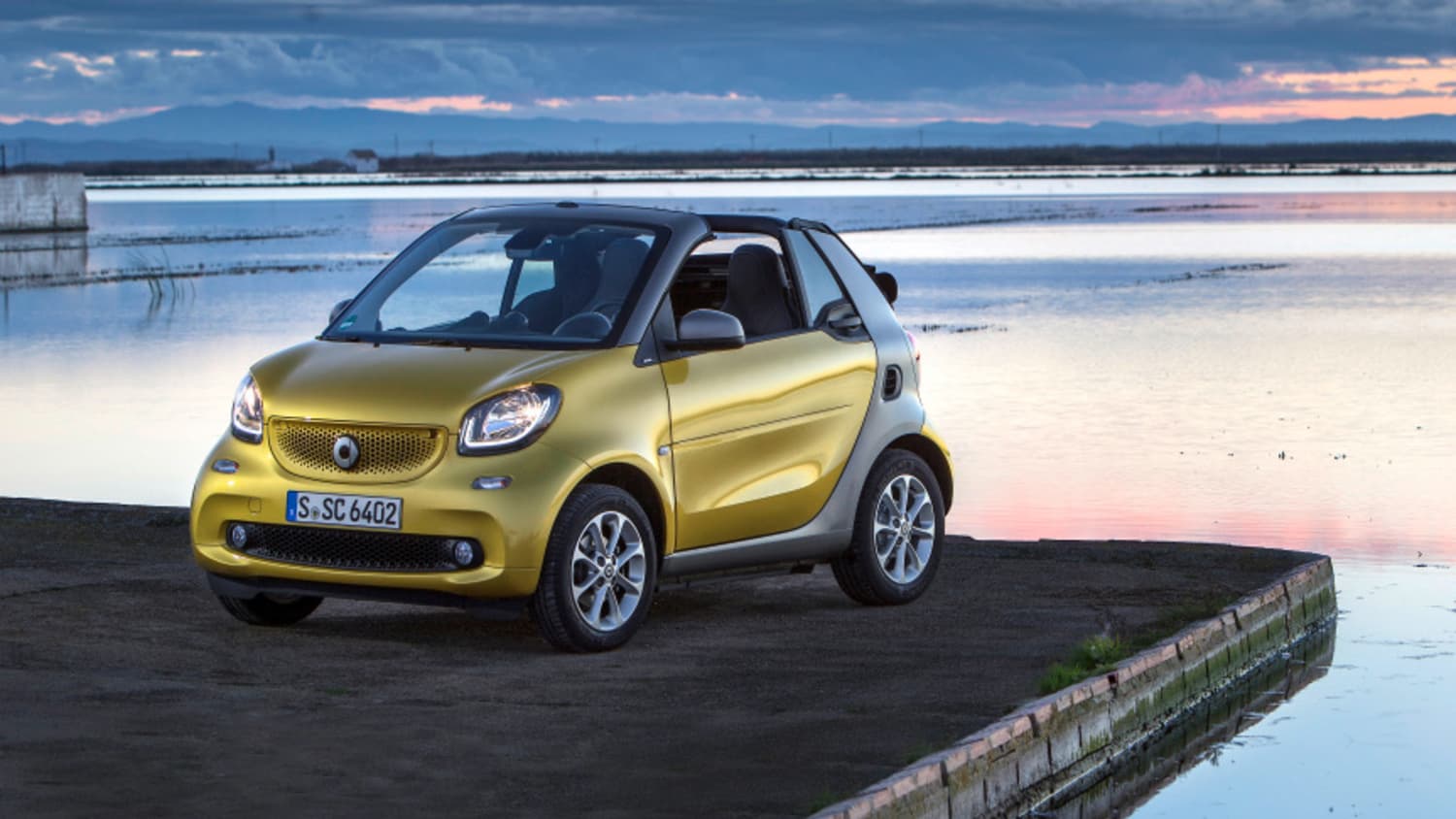 gelber Smart Fortwo steht auf einem Parkplatz am See