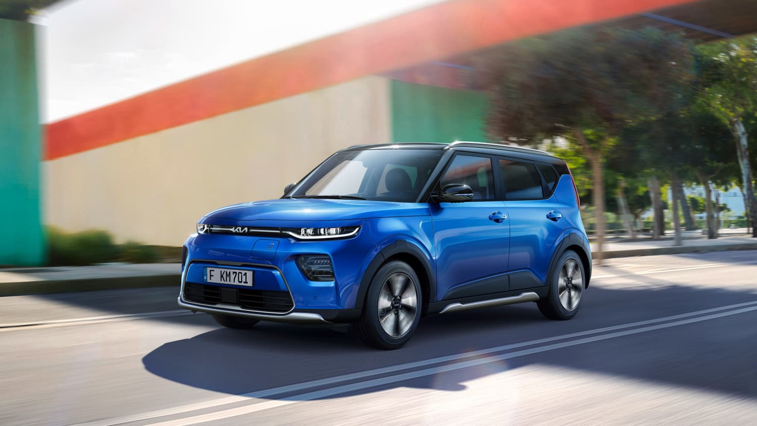 Der neue Kia e-Soul in Blau während der Fahrt unter einer grün-roten Brücke