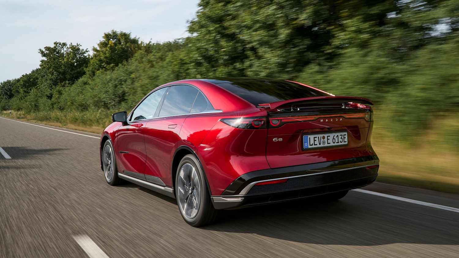 Der fahrende Mazda 6e von hinten auf einer Landstraße am Meer