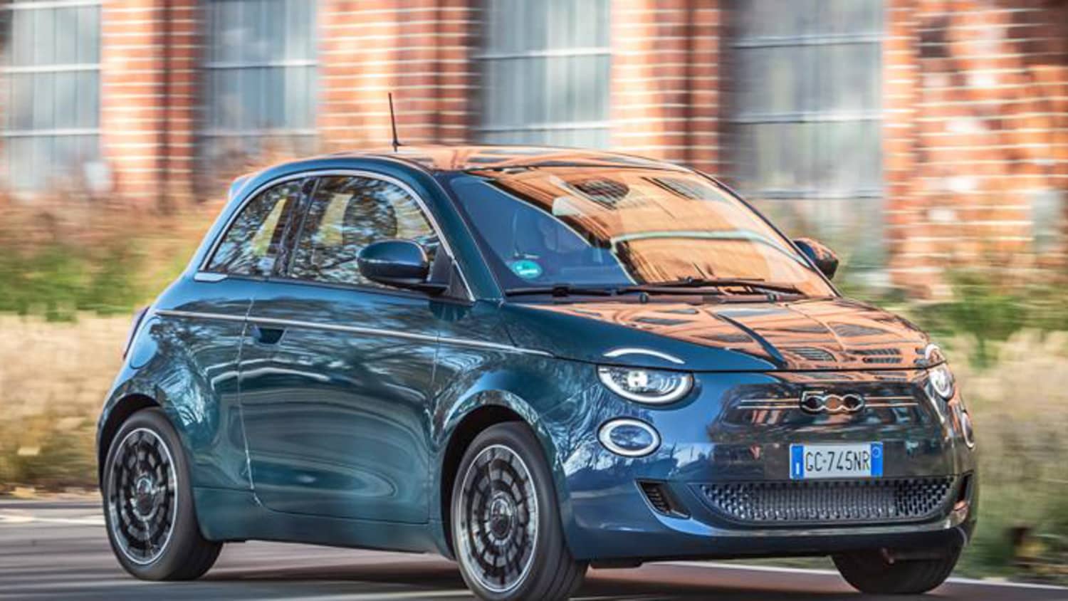 Ein Fiat 500 E fährt an einem Backsteingebäude vorbei