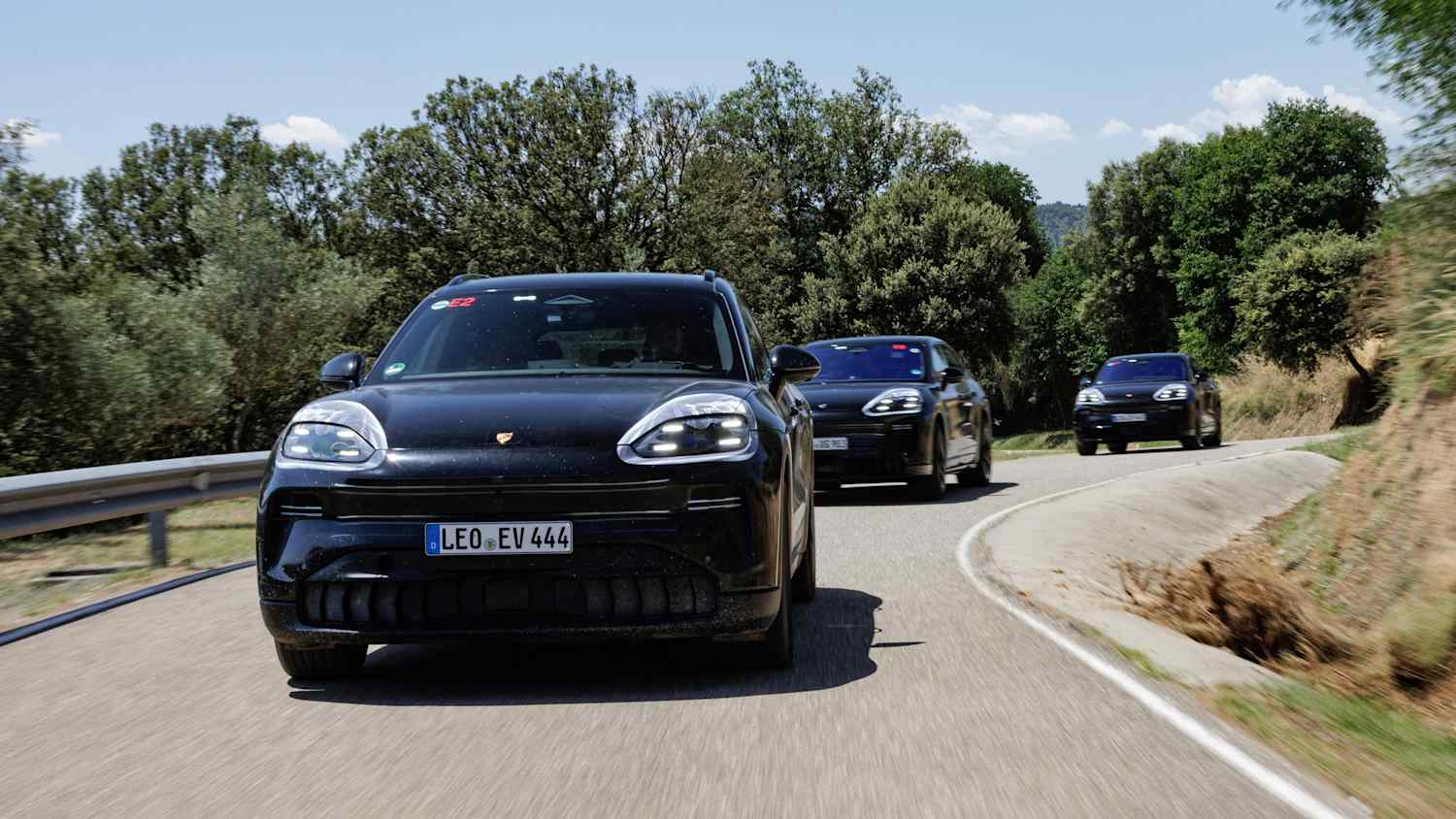Frontansicht drei fahrender Porsche Cayenne E auf einer Landstraße bei sonnigem Wetter