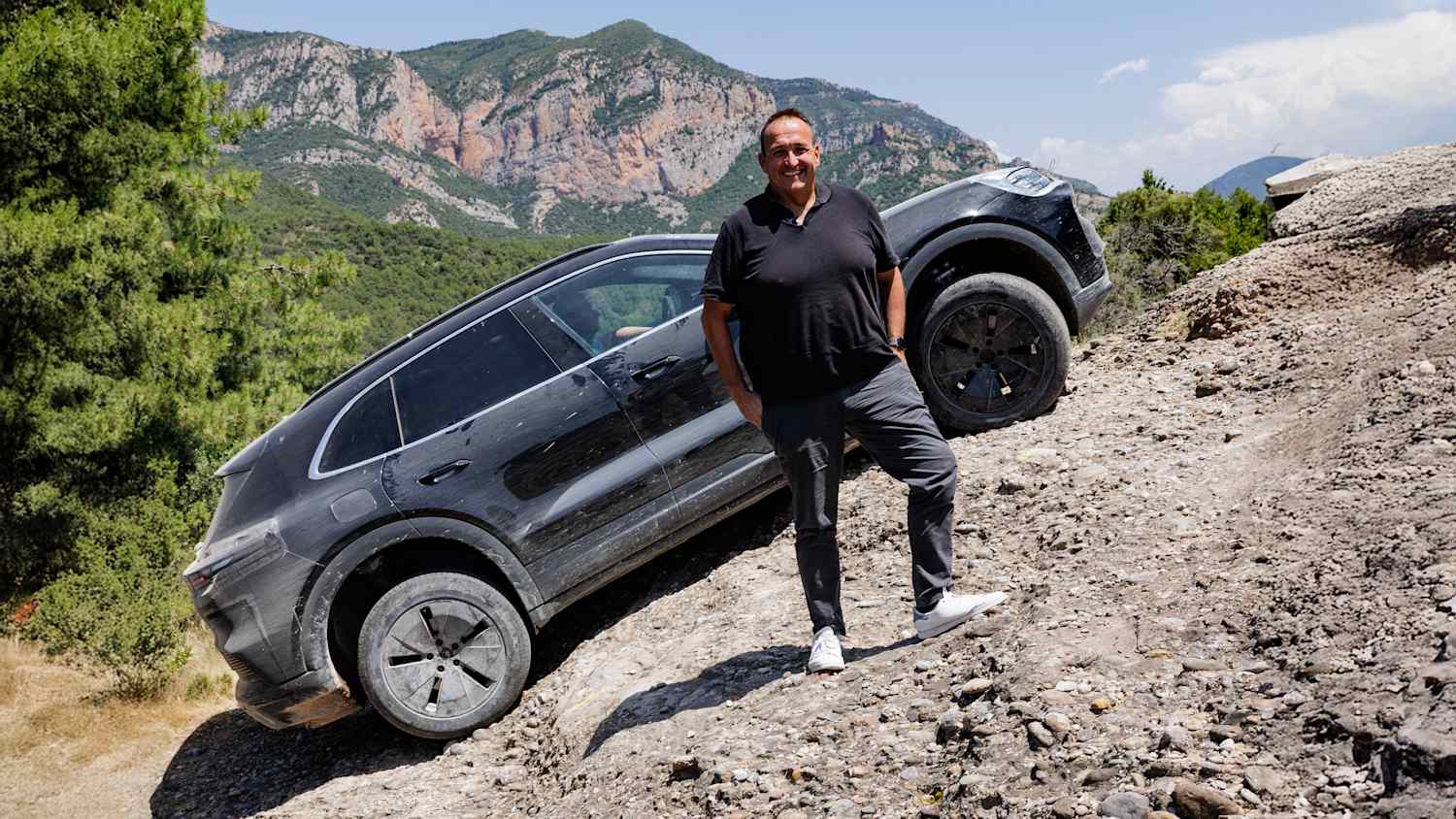 Thomas Geiger steht neben einem geparkten Porsche Cayenne E auf einem Feldweg.