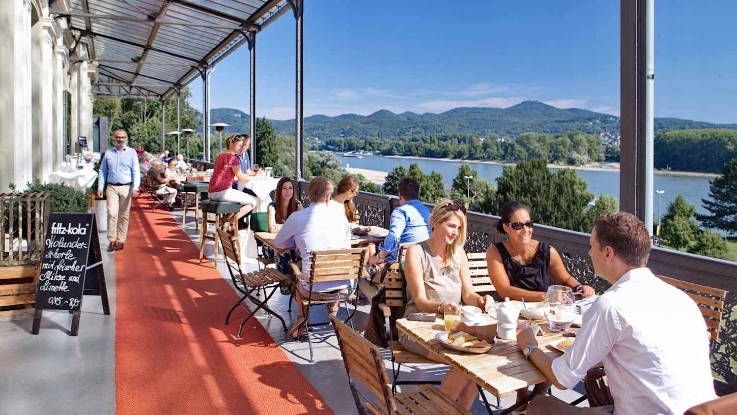 Menschen sitzen auf der Nordterrasse am Bahnhof Rolandseck mit Blick auf den Rhein