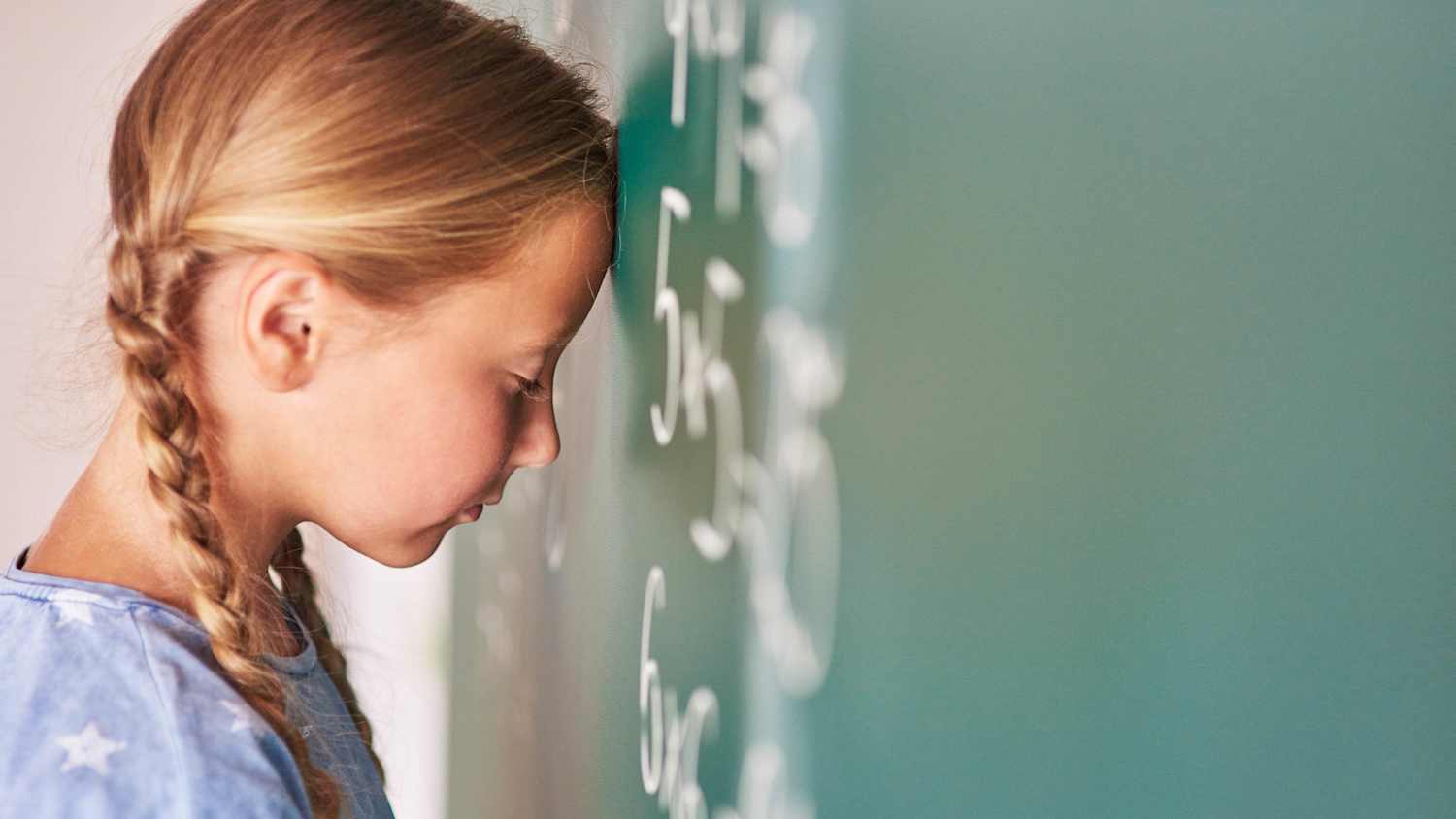 Ein Schulmädchen lehnt mit ihrem Kopf an der Tafel