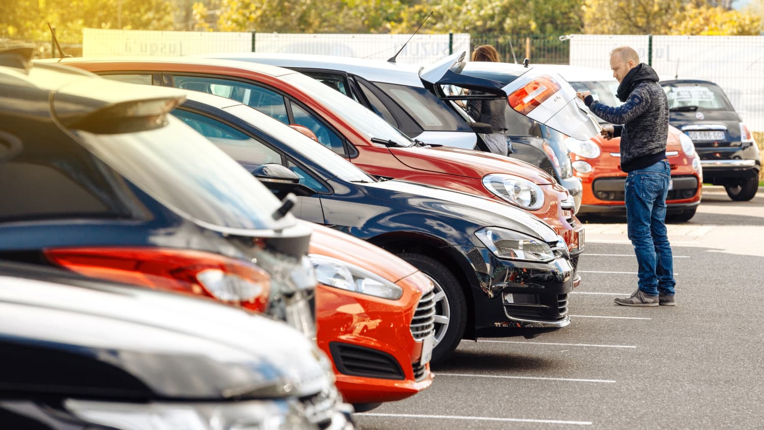 Ein Mann checkt den Kofferraum eines Gebrauchtwagen auf einem Hof mit vielen Autos