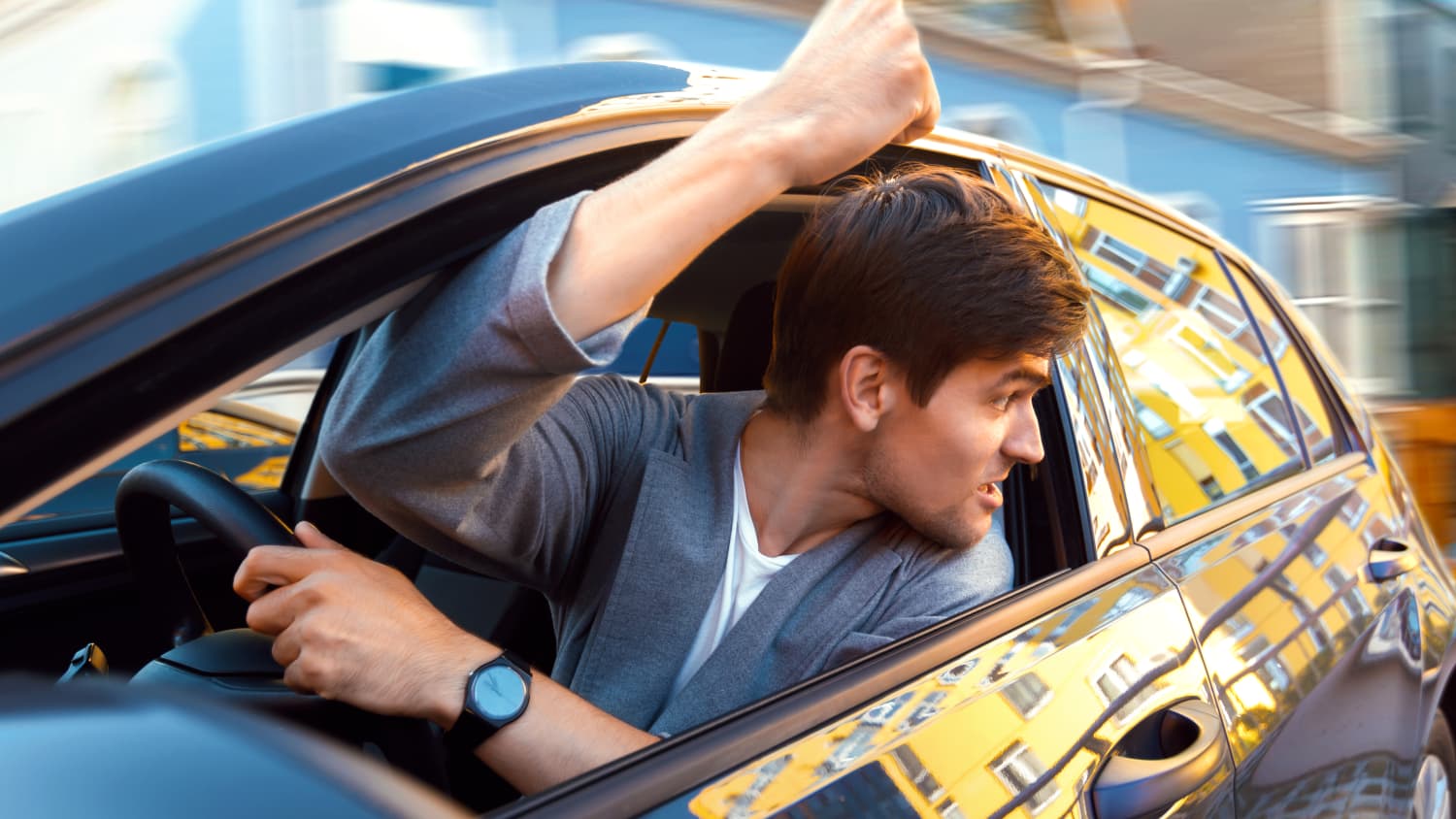 Ein aggressiver Mann am Steuer schimpft mit erhobener Faust aus dem Autofenster im Straßenverkehr
