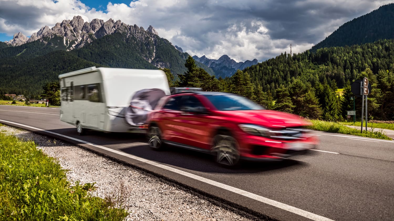 Ein rotes Auto zieht einen Wohnwagen vor einer Bergkulisse