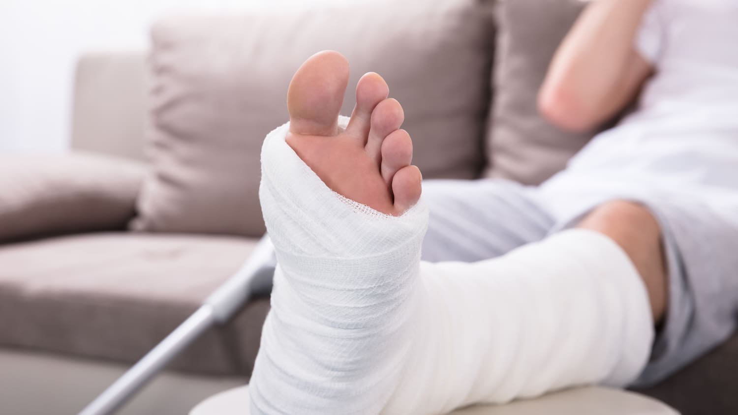 Man mit einem Gipsbein sitzt auf einem Sofa.