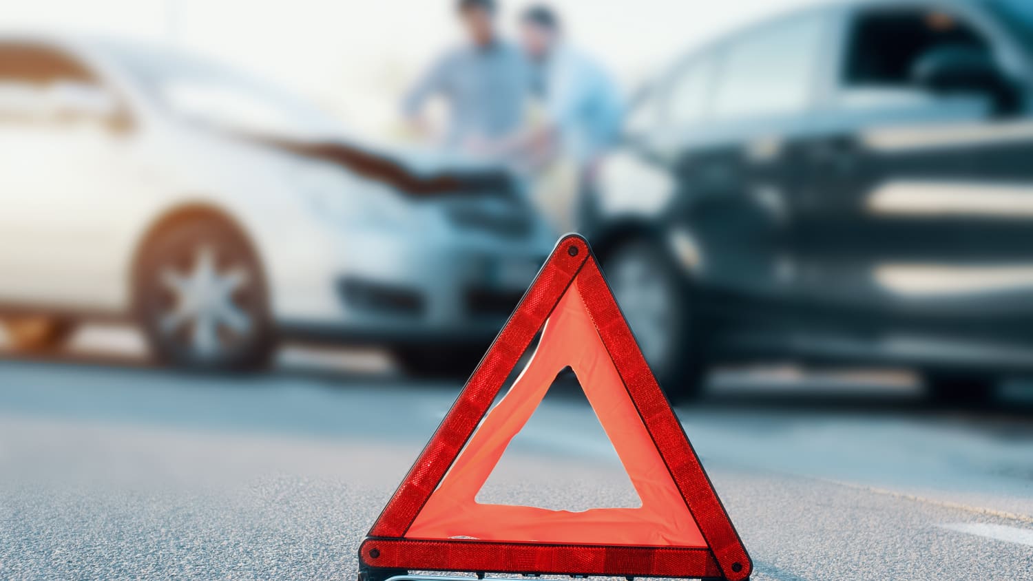 Ein Warndreieck auf einer Strasse, im Hintergrund ein Unfall