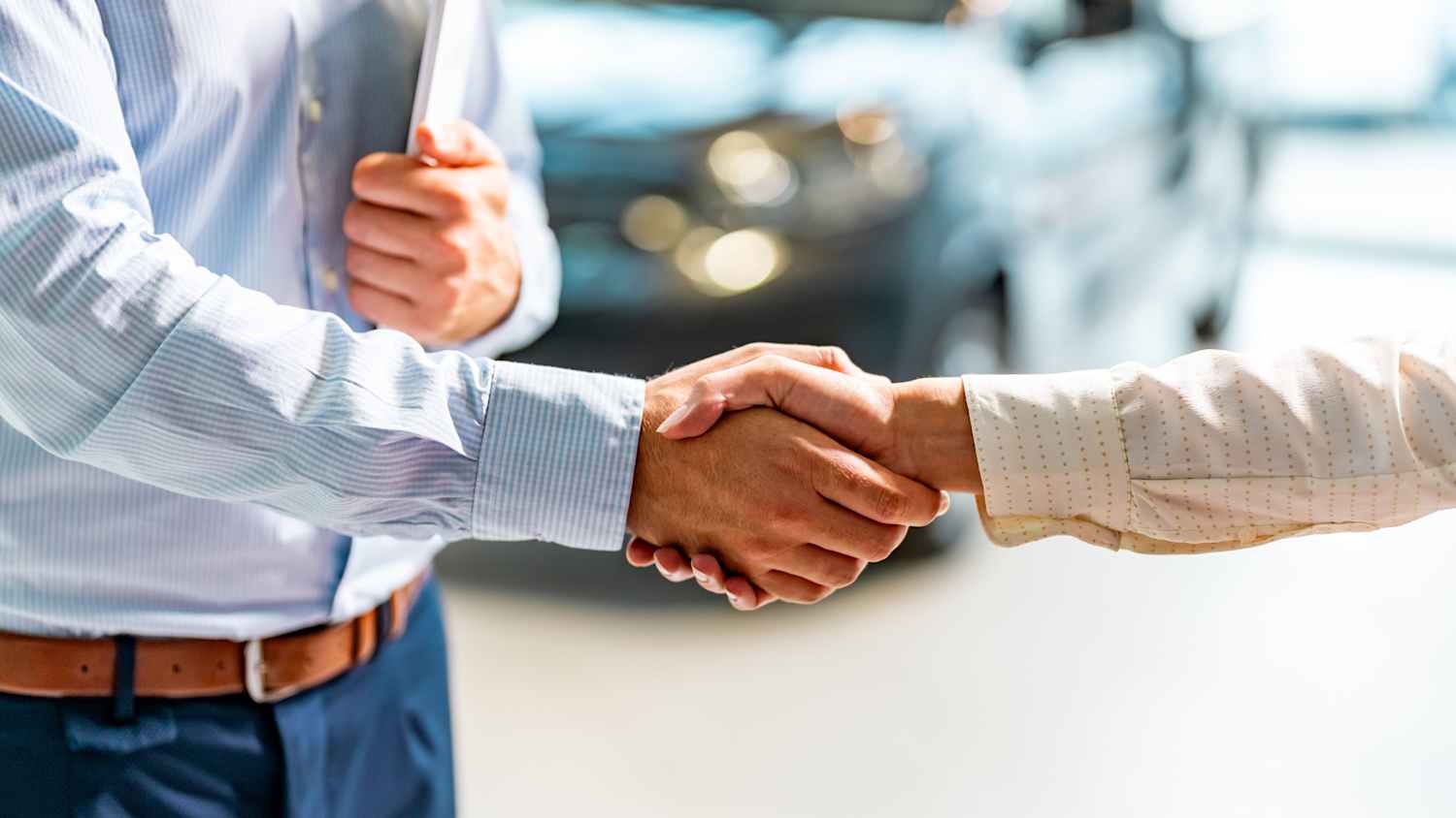Ein Autoverkäufer im Autohaus gibt dem Kunden die Hand nach Vertragsabschluss