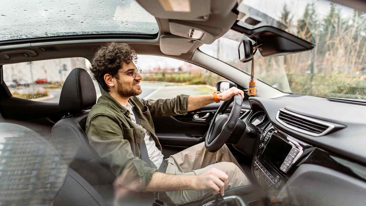 Junger lächelnder Mann konzentriert sich auf die Straße beim Autofahren durch die Stadt