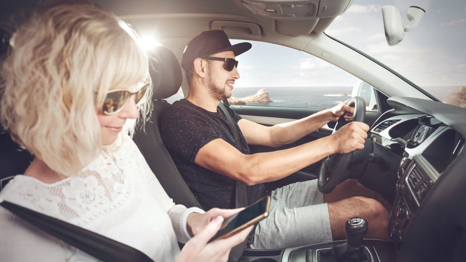 Ein Mann und eine Frau sitzen in einem Auto, der Mann fährt, die Frau ist am Handy