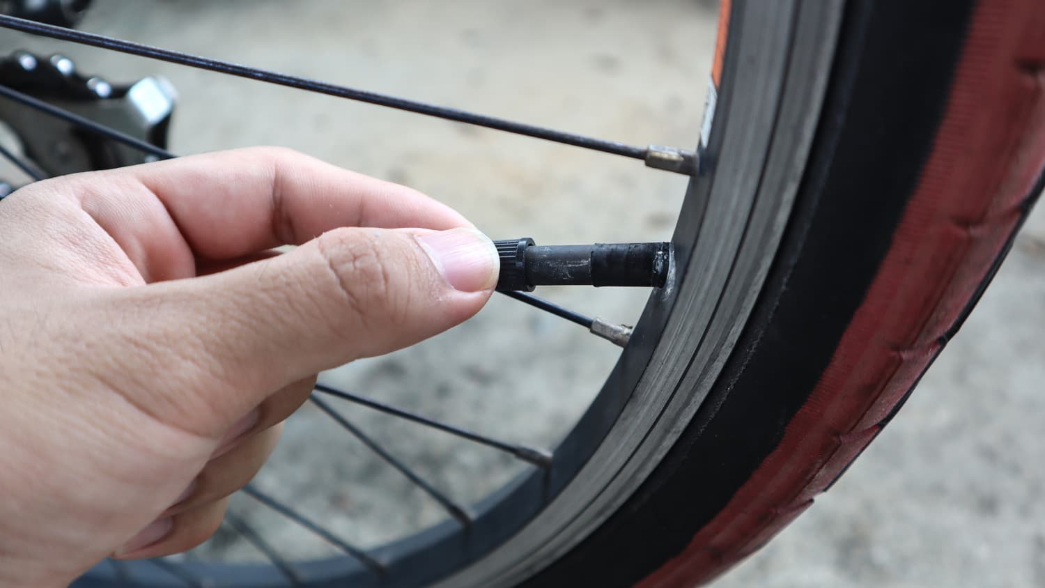 Eine Hand hält ein abgebrochenes Fahrradventil am Rad eines Fahrrades