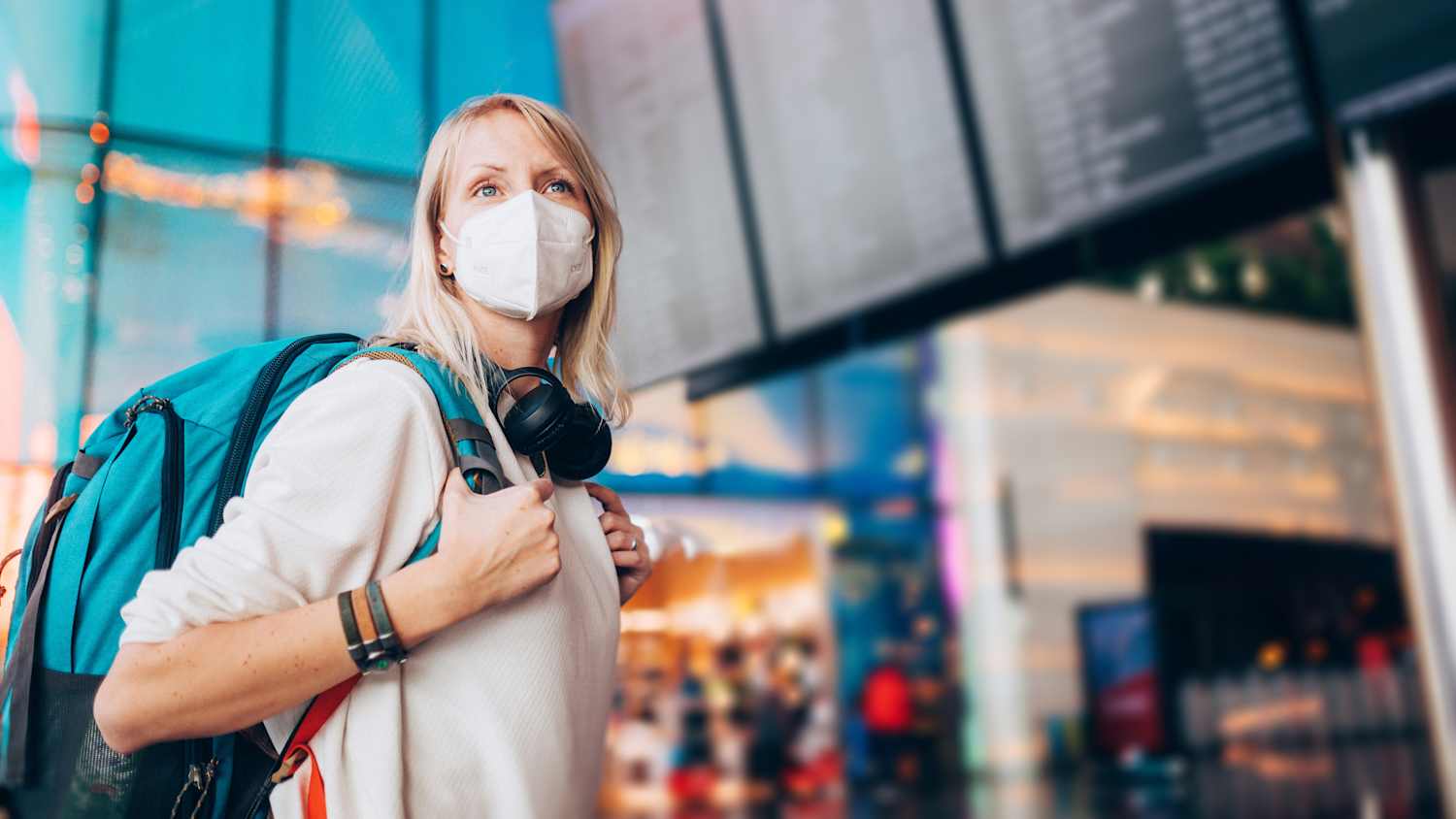 Eine blonde Frau mit Rucksack auf dem Rücken trägt eine Maske an einem Flughafen