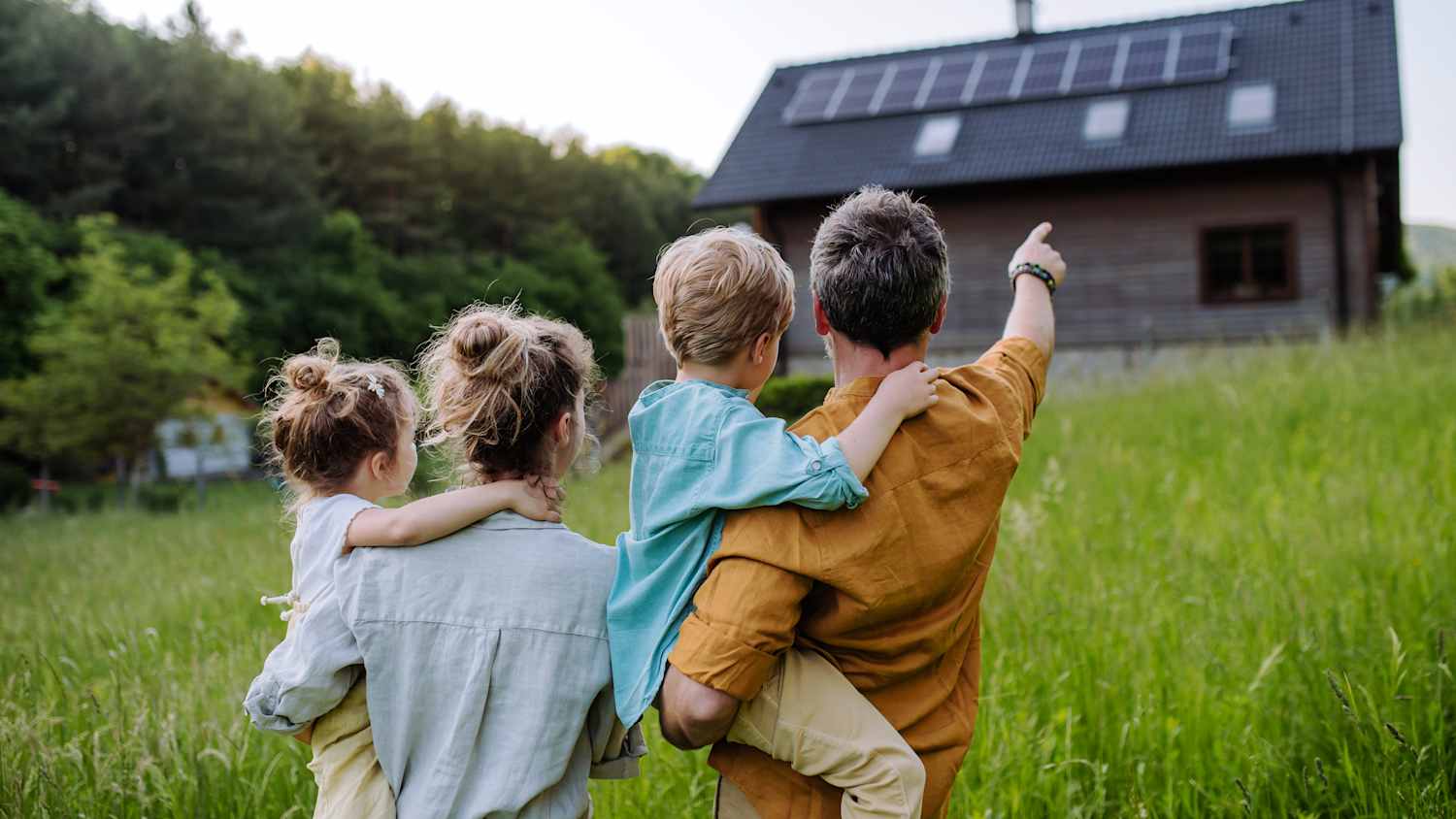 Ein Familienvater zeigt seiner Frau und den beiden Kindern die PV Anlage auf dem Hausdach