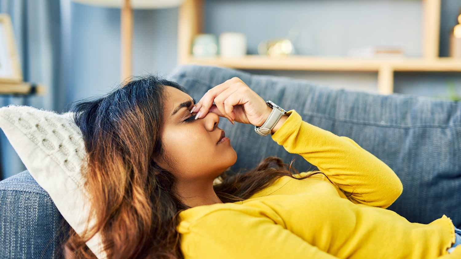 Eine junge Frau entspannt auf dem Sofa und massiert sich den Nasenrücken