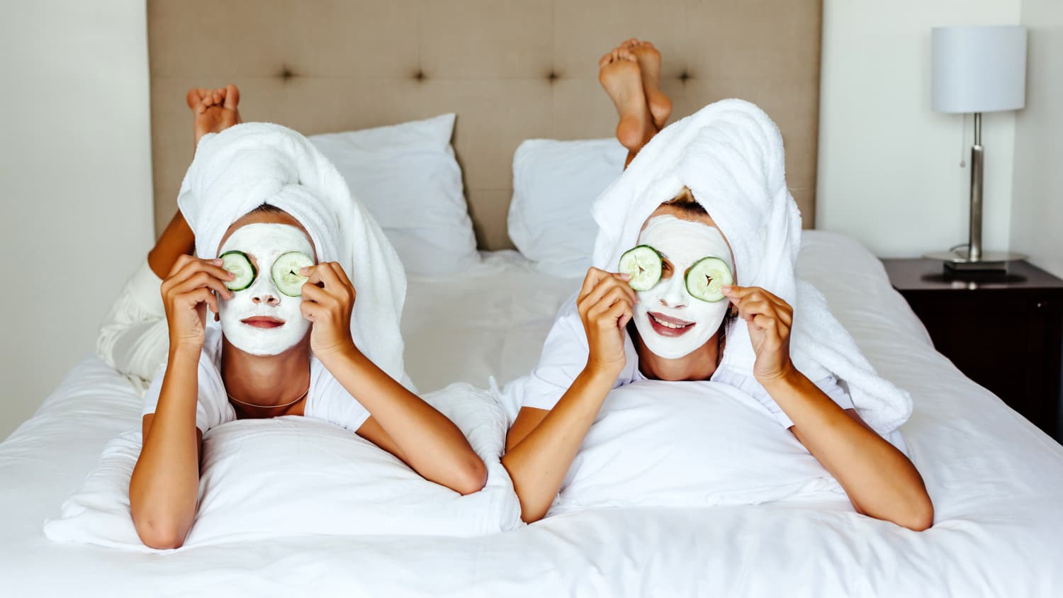 Mutter und Tochter liegen auf einem Hotelbett mit Gesichtsmasken und Gurkenscheiben