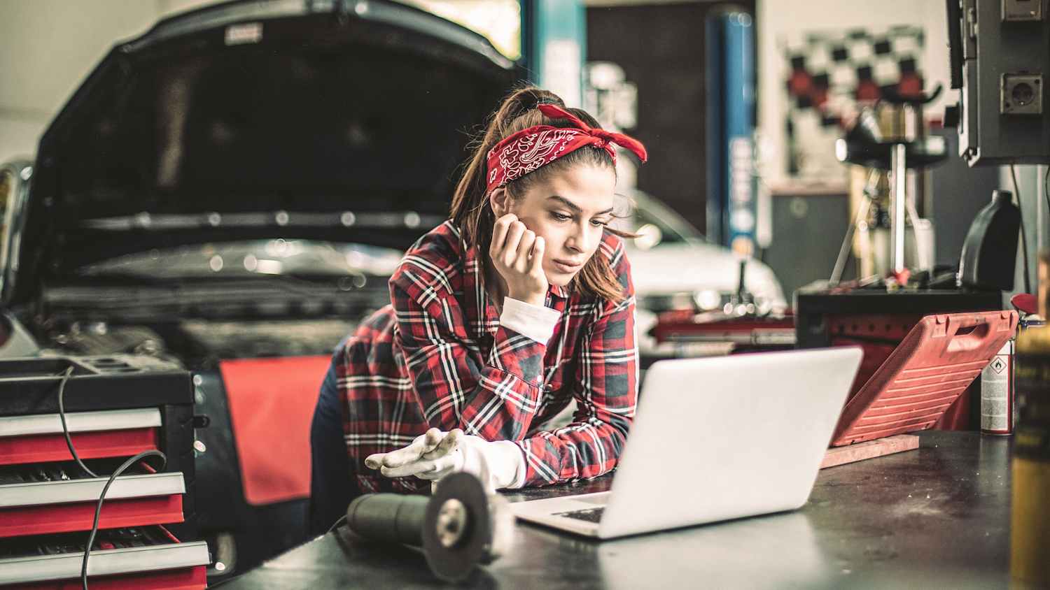 EIne Frau schaut auf ihrem Laptop ein Erklärvideo in einer Autowerkstatt