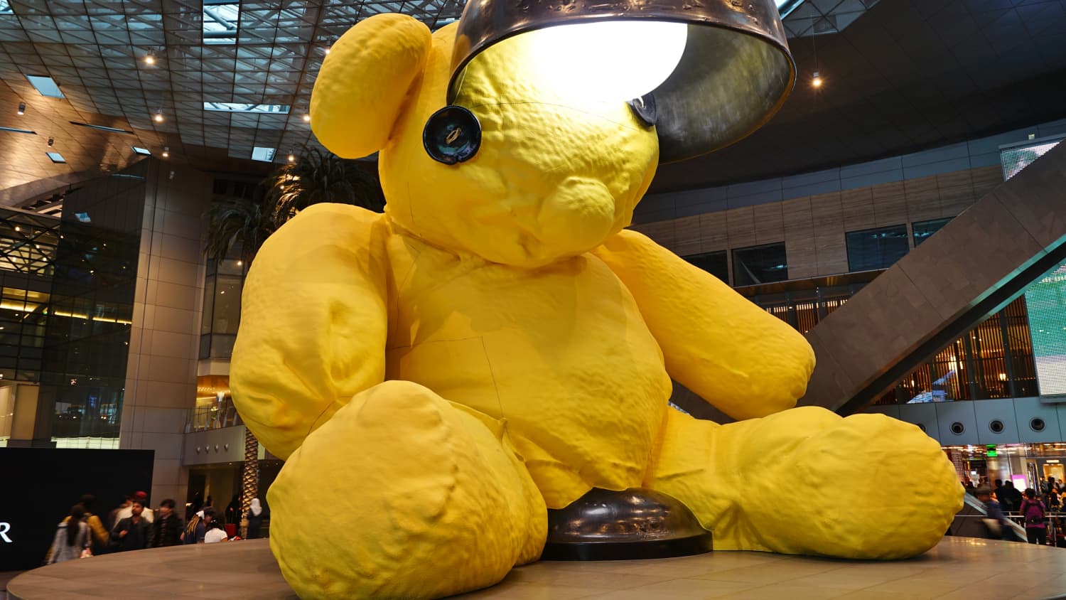 Ein riesiger gelber Bär mit einem Lampenschirm am Kopf im Flughafen von Doha