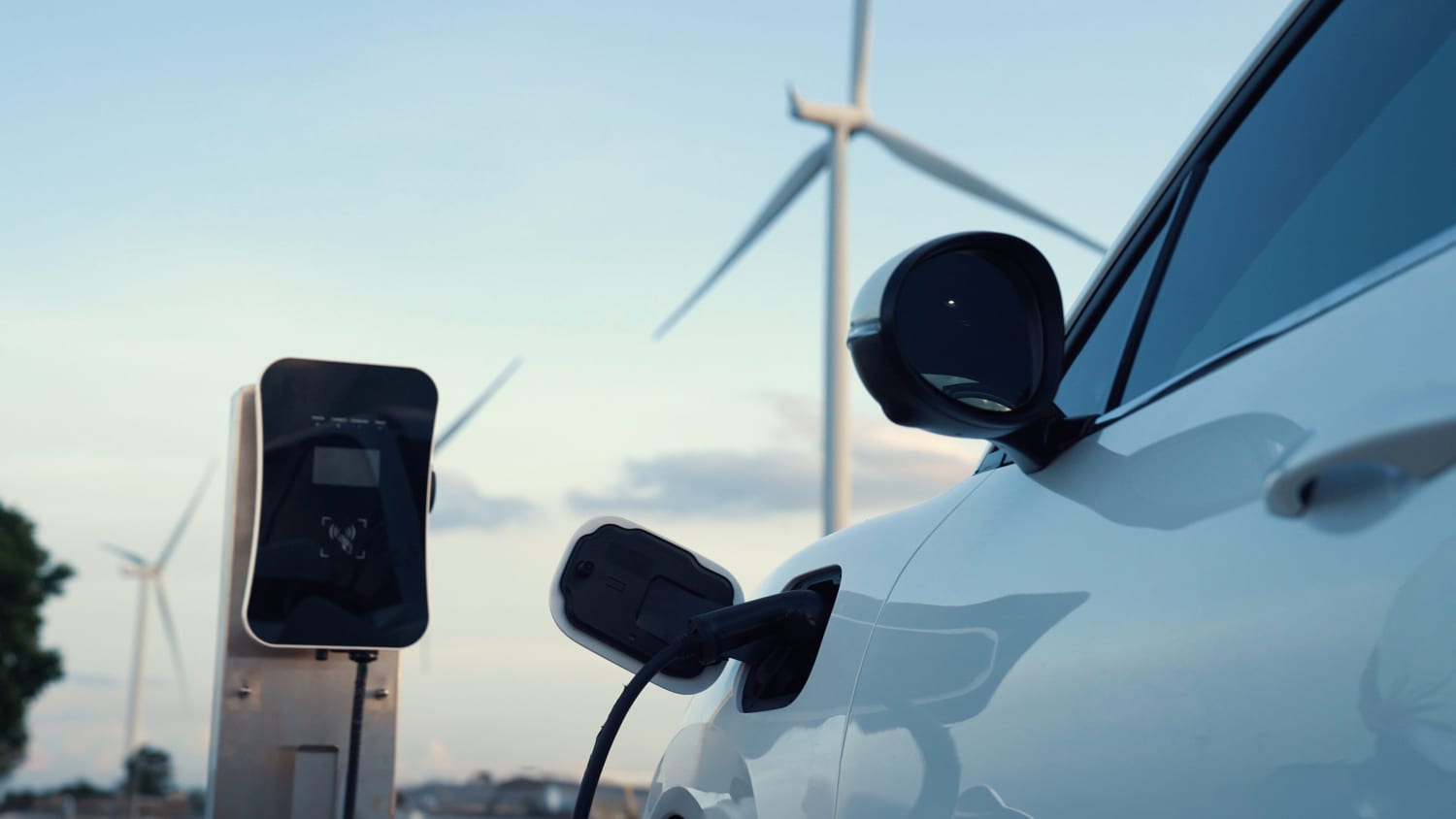 Ein Elektroauto lädt an einer Ladesäule. Im Hintergrund sind Windräder zu sehen.