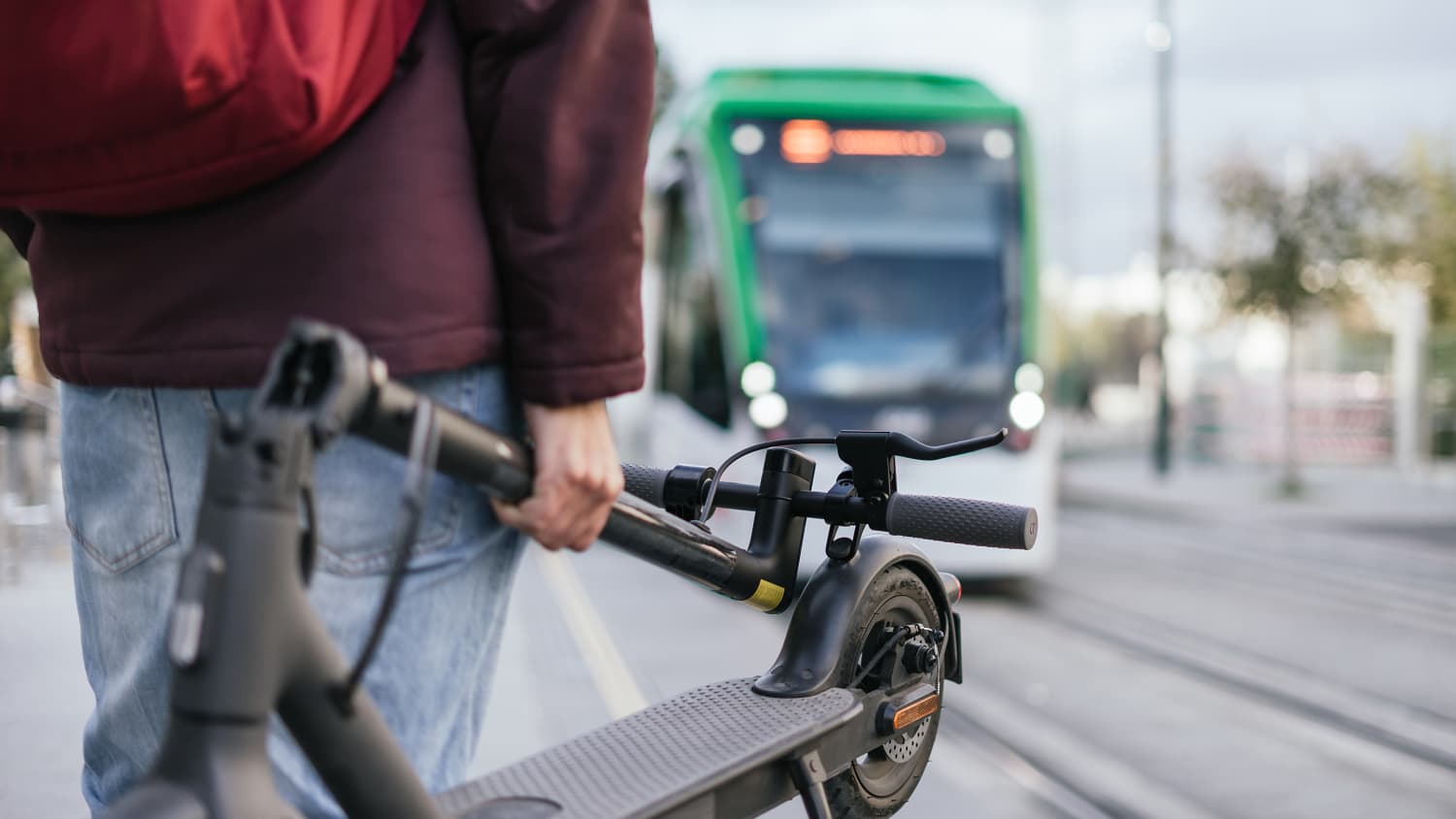 Eine Frau wartet mit ihrem Elektro-Roller in der Hand auf die Bahn
