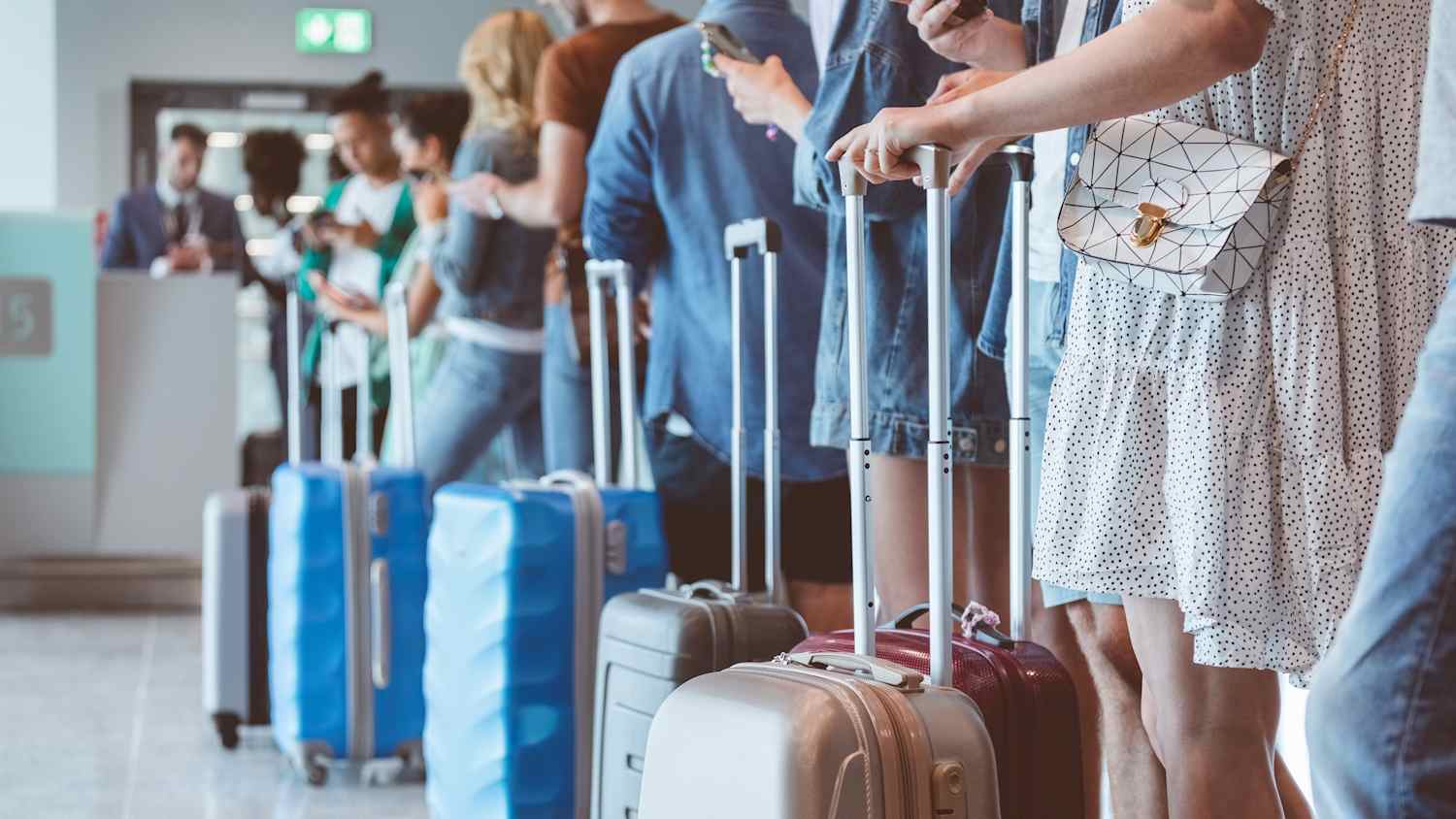 Reisende mit Gepäck benutzen Smartphones, während sie am Flughafen in der Schlange für das Boarding warten. Konzentrieren Sie sich auf Rollgepäck.