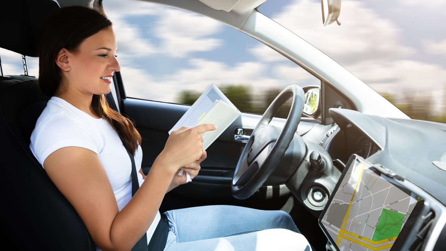 Frau liest ein Buch am Steuer eines Autos, das autonom fährt