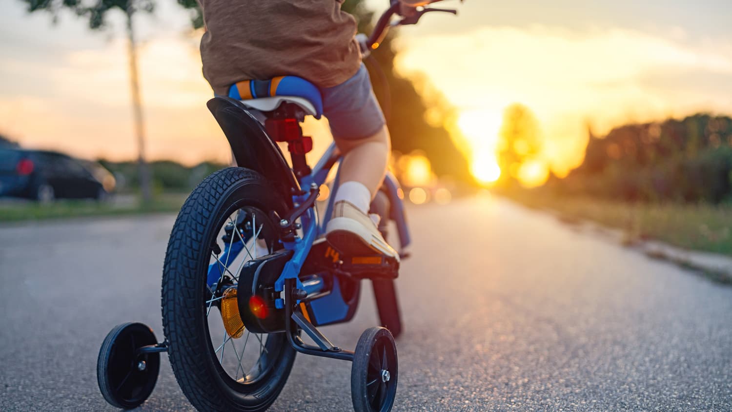 Ein Kind radelt mit seinen Fahrrad mit Stützrädern in den Sonnenuntergang