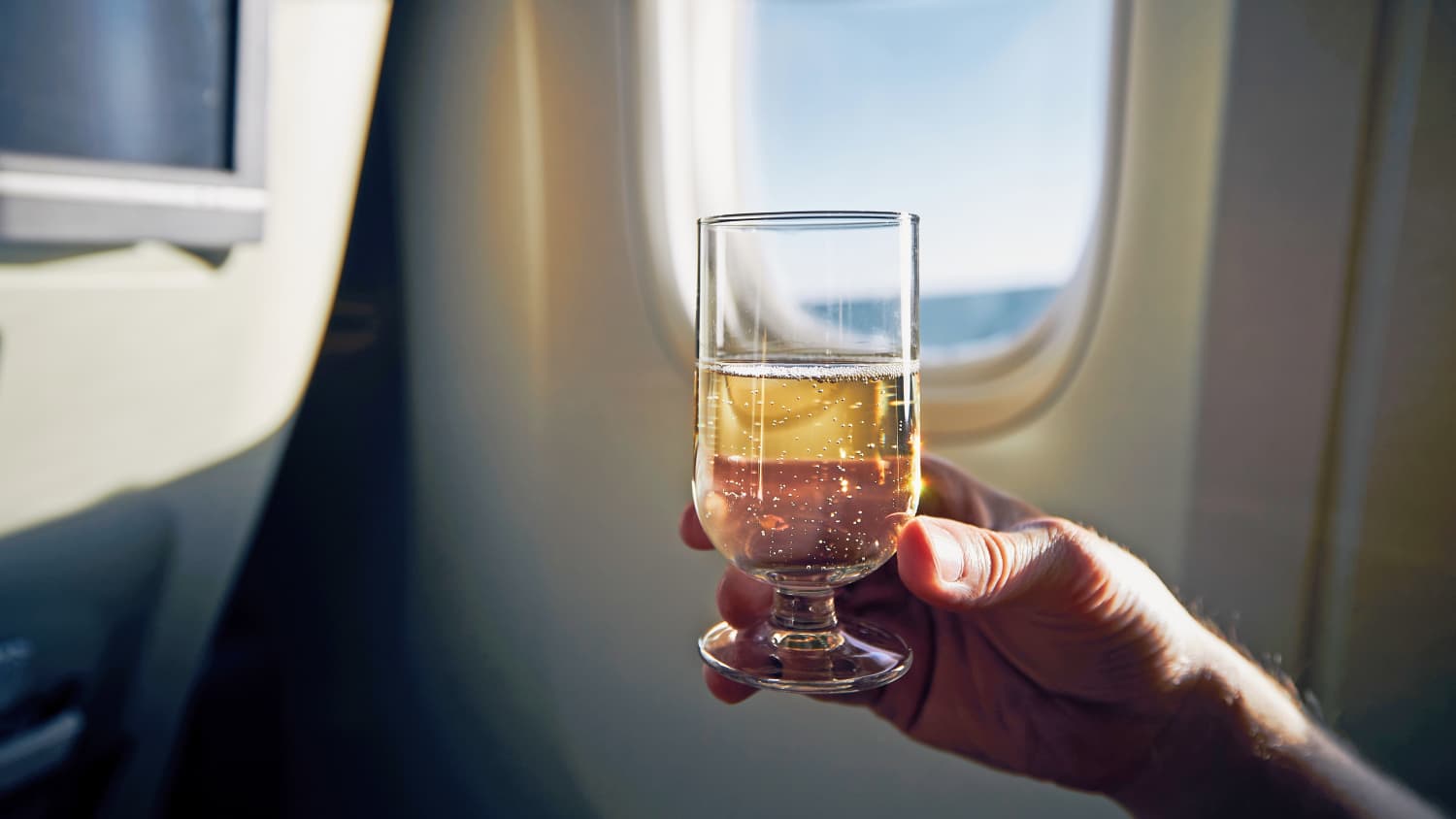 Eine Person hält ein Glas Wein im Flugzeug in der Hand