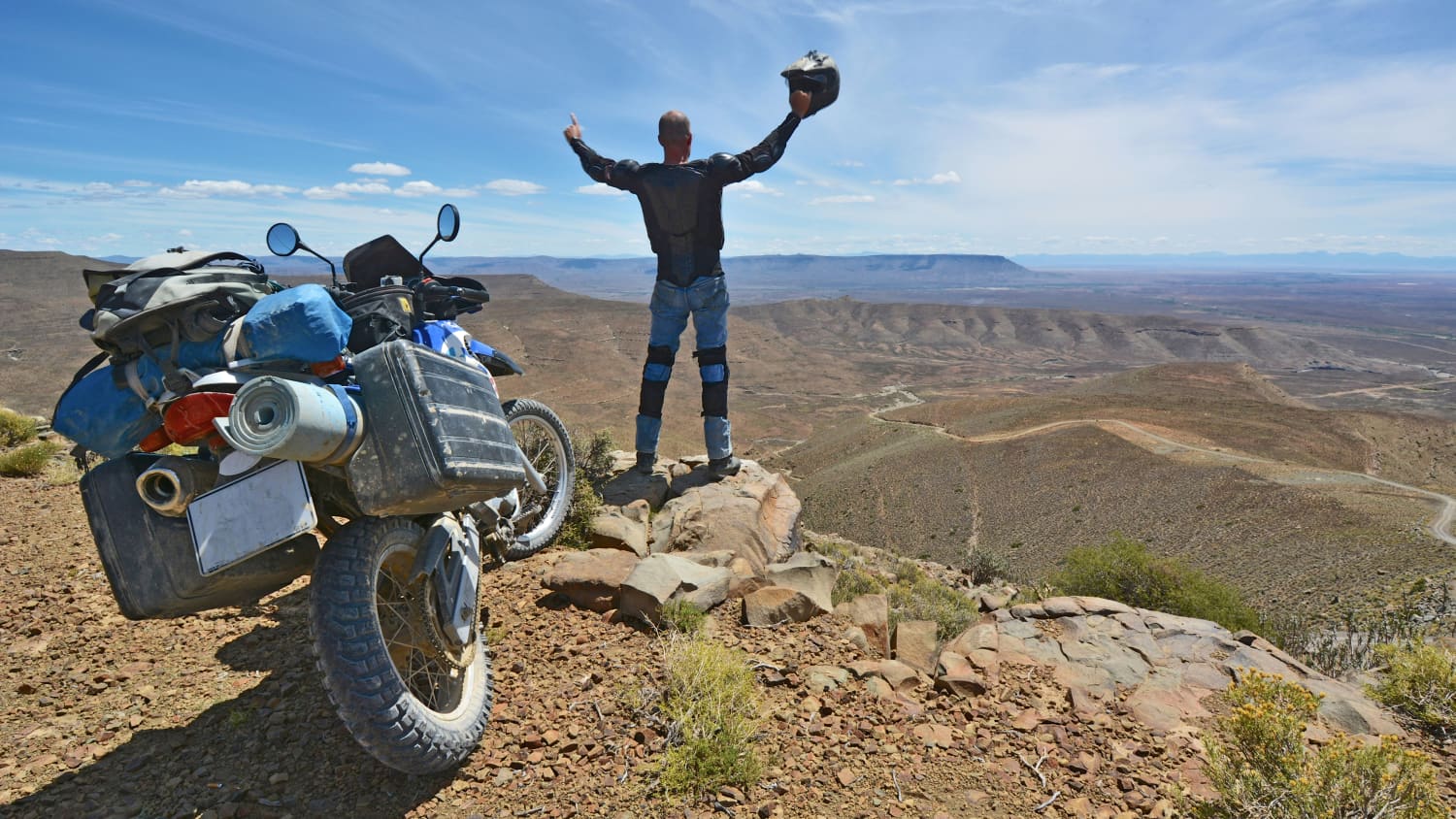 Ein Mann schaut über ein Tal und freut sich im Hintergrund parkt sein Motorrad