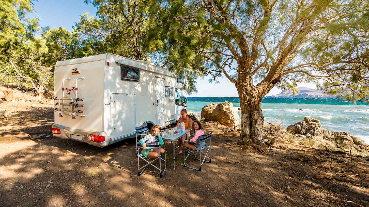 Eine Familie steht mit ihrem Wohnmobil in Griechenland mit Ausblick aufs Meer
