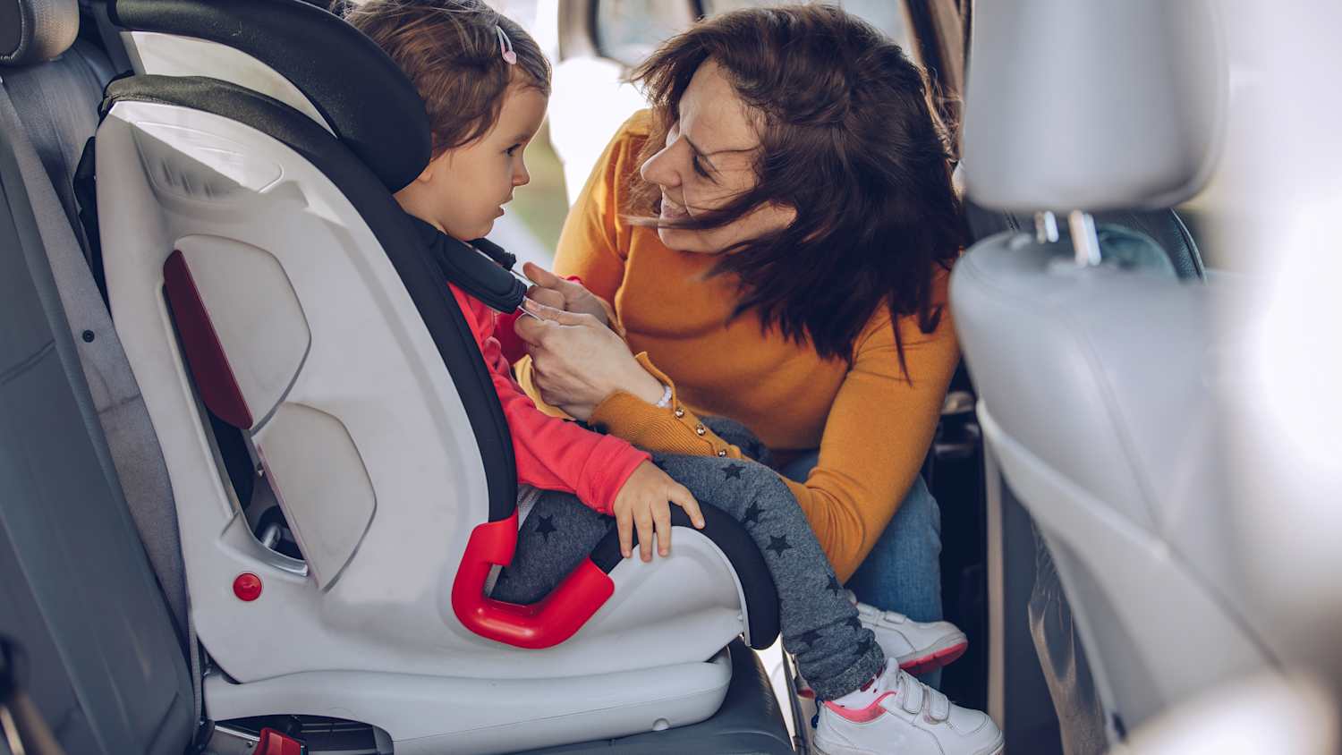 Eine Mutter schnallt ihr Kind im Kindersitz auf der Rückbank eines Autos an