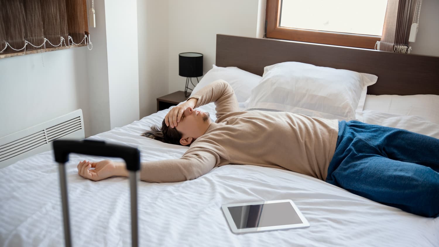 Ein Mann liegt krank auf einem Hotelbett