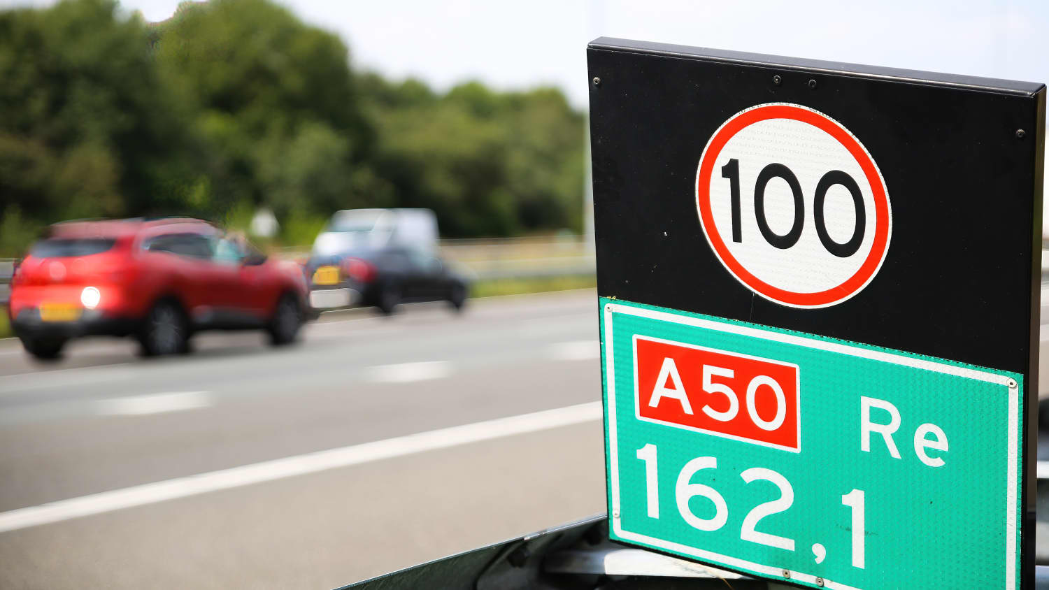 Nahaufnahme des Tempolimits 100 an der holländischen Autobahn, unscharfer Autohintergrund