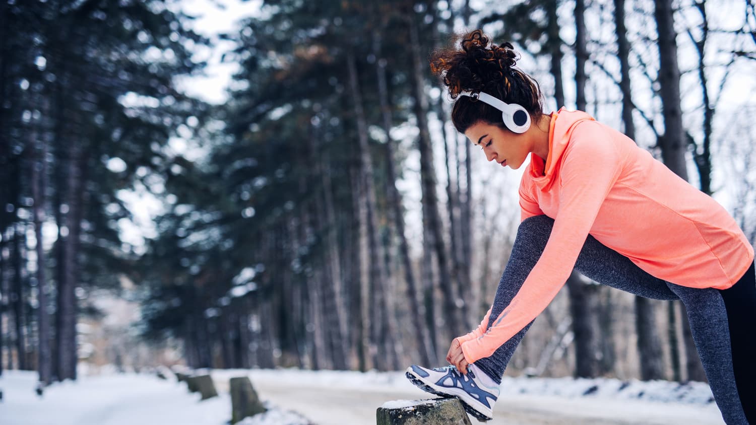 Eine Frau bindet sich die Turnschuhe während einer Jogging-Runde im Wald im Winter