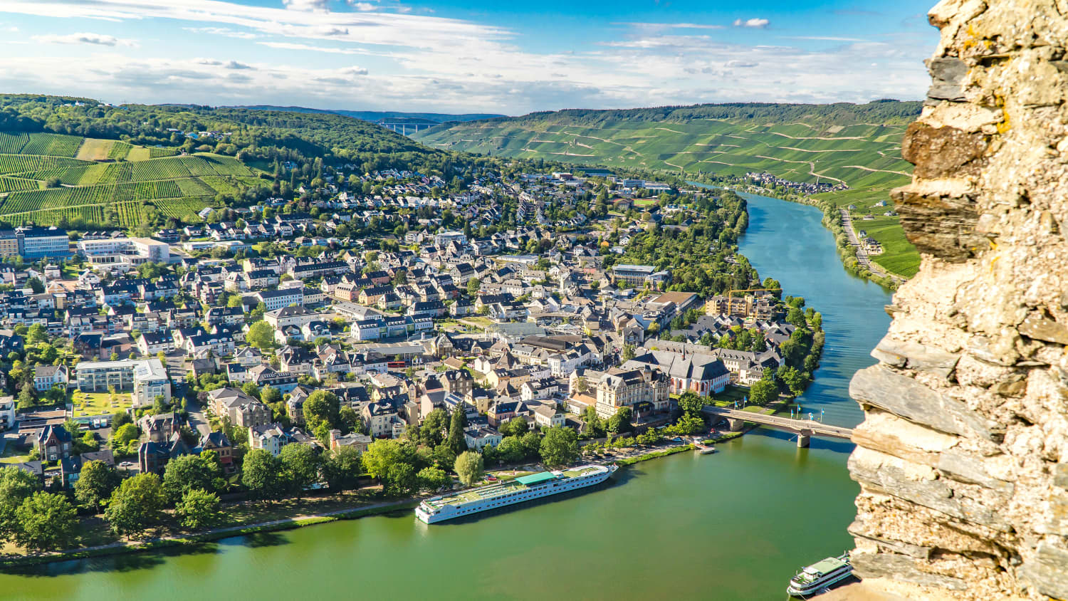 Blick von einem Berg auf einen Fluss mit Schiffen und am Ufer ist eine Stadt zu sehen