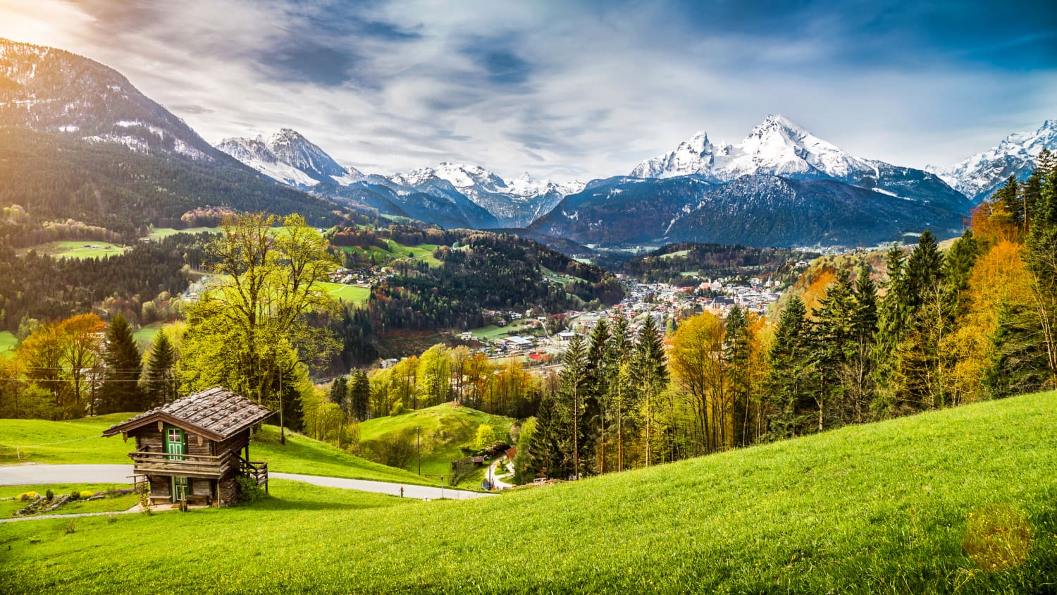 Blick über Wiesen und Wälder auf eine schneebedeckte Bergkette