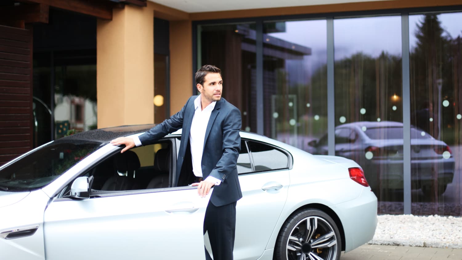 Attraktiver Mann steht an der geöffneten Türe eines silbernen BMW