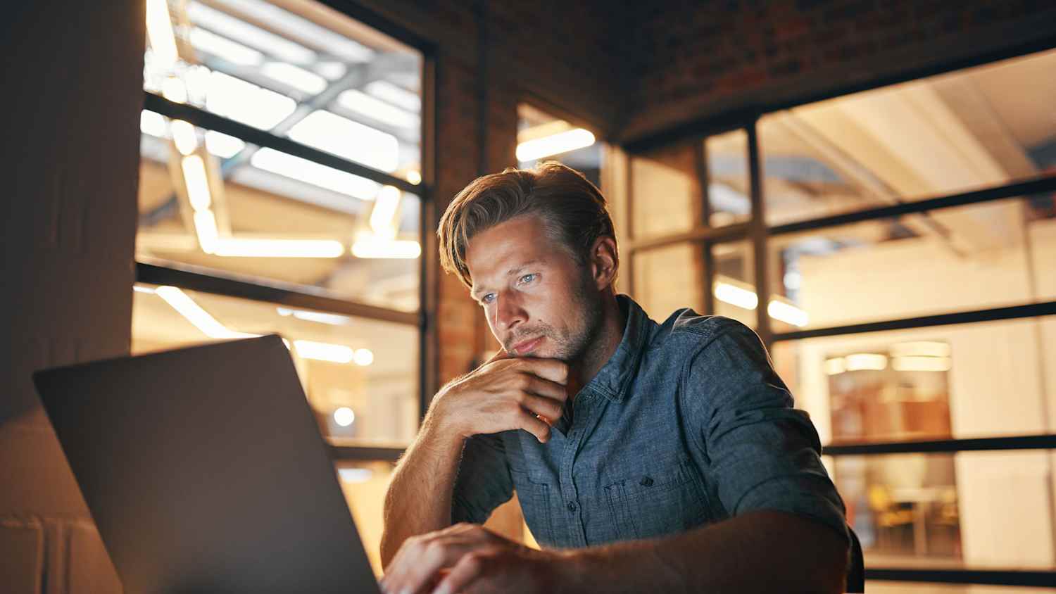 An Mann sitzt am Schreitisch und arbeitet am Labtop