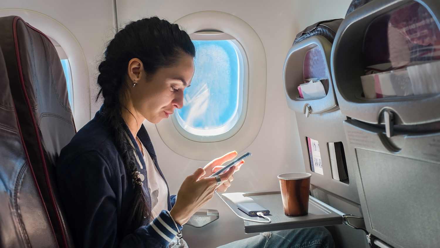 Eine Frau läd ihr Handy mit einer Powerbank im Flugzeug