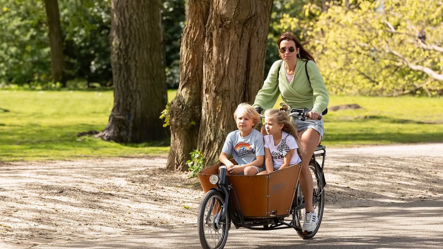 Eine Frau fährt mit ihrem Babboe Lastenrad durch den Park